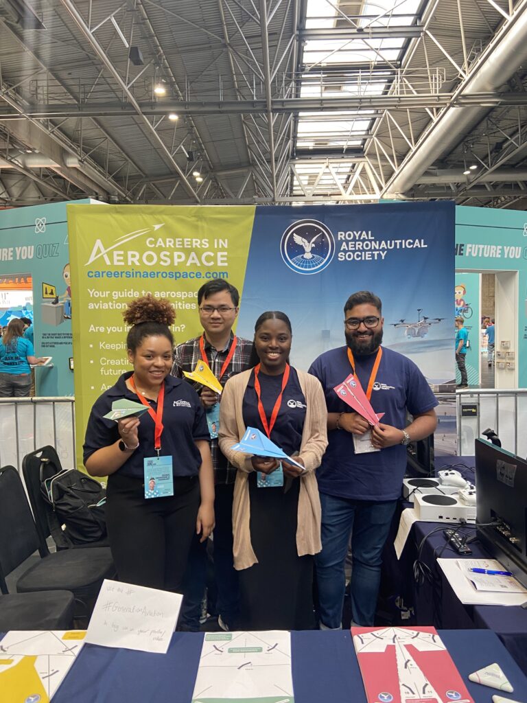 4 volunteers for the RAeS holding paper planes in front of a big careers in aerospace banner