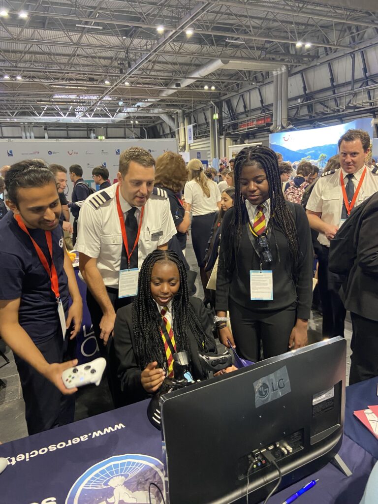 A pilot and a RAeS Volunteer helping a young women fly a plane in a simulator
